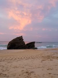 Rock formation on beach against sky during sunset