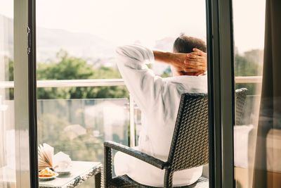 Side view of man relaxing by window at home