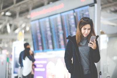 Young woman using phone while standing on laptop