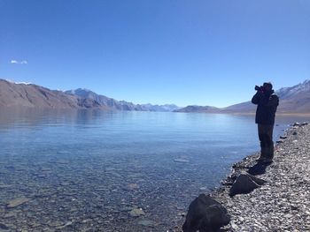 Man photographing at shore against clear sky