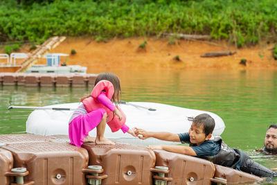 Girl holding boy hand on raft with father in lake 