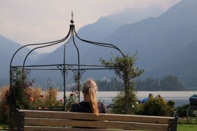 Rear view of woman sitting on railing against mountains