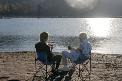 Senior man and his daughter relaxing together sitting outdoors near a lake in nature.