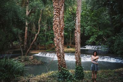 Multiple exposure of woman standing by tree in forest against river