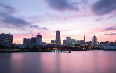 Sea by modern buildings against sky at sunset