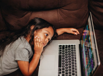 Cute girl using laptop while lying on sofa at home