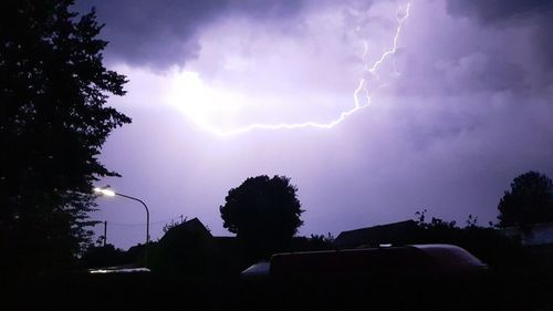 Lightning over silhouette trees against sky at dusk