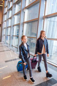 Full length of sisters with luggage walking at airport