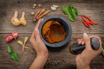 Cropped hands preparing food in mortar and pestle on wooden table