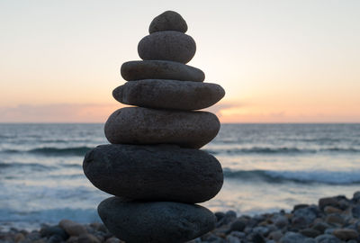 Stack of pebbles at beach against sky during sunset