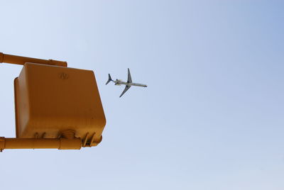 Low angle view of airplane flying over stoplight against clear sky