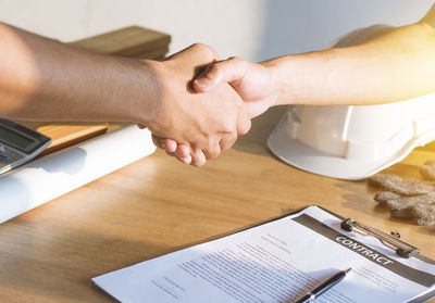 Cropped image of colleagues giving handshake over contract paper in office