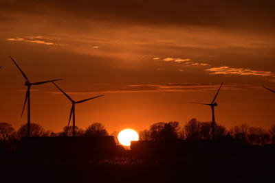 Silhouette wind turbines on field against sky during sunset