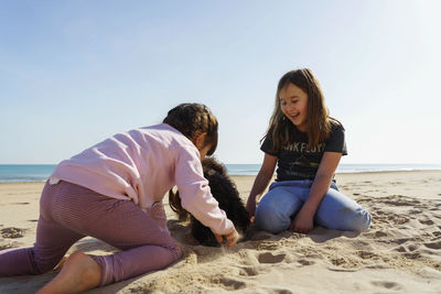 Two girls  sitting on beach and playing with dog