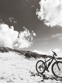 Bicycle on snow covered field against sky