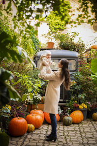 Woman playing with daughter while standing by pumpkins against trees