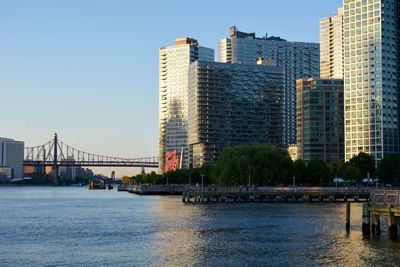 Bridge over river by buildings in city against clear sky