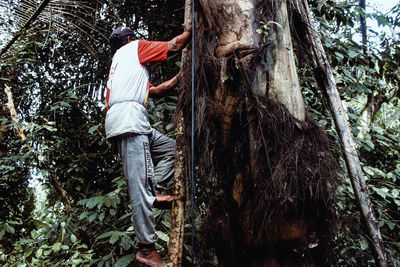 Side view of man standing by tree trunk in forest