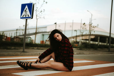 Young woman sitting on road against sky