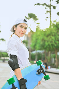 Portrait of woman holding skateboard while standing outdoors