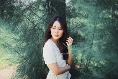 Beautiful young woman looking down by trees in forest