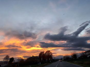 Cars on road against dramatic sky during sunset