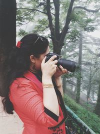 Young woman using mobile phone while standing on tree in forest