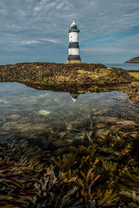 Lighthouse by sea against sky