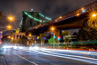 Light trails on street by brooklyn bridge in manhattan at night