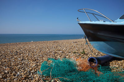 Turquoise and orange fishing net on a shingle beach next to a fishing boat with clear blue sky