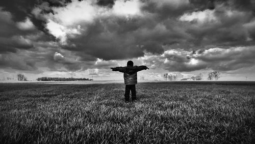 Man standing on grassy field against cloudy sky