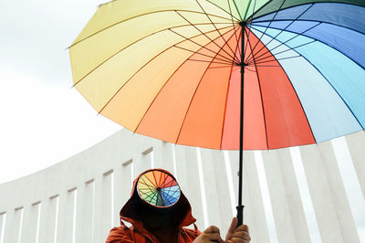 Low angle view of people holding multi colored umbrella against sky