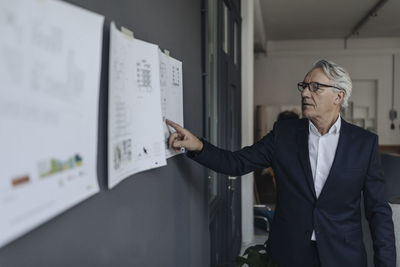 Senior businessman looking at papers hanging on the wall