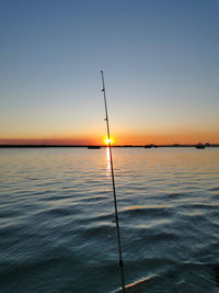 Fishing rod over sea against sky during sunset
