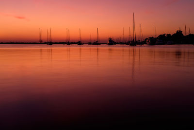 Silhouette sailboats moored in sea against sky during sunset