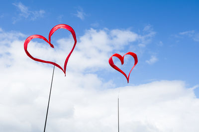 Low angle view of red heart shape against sky