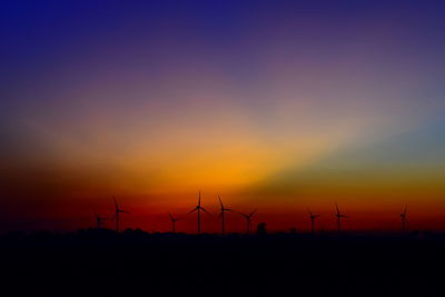 Silhouette wind turbines on field against sky during sunset