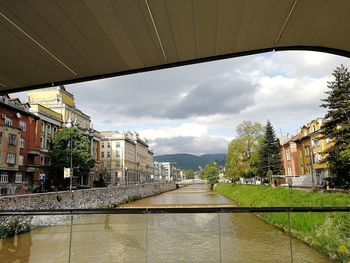 Bridge over river amidst buildings in city against sky