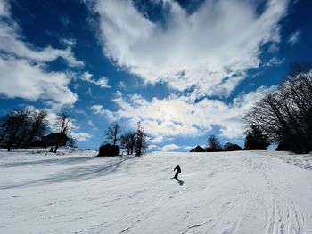 Lonely skier going down the slope on a sunny day with white fluffy clouds