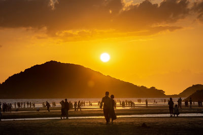 Silhouette people on mountain by sea against sky during sunset