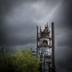 Low angle view of factory against cloudy sky