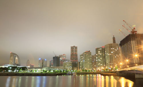 Illuminated buildings by river against sky in city at night