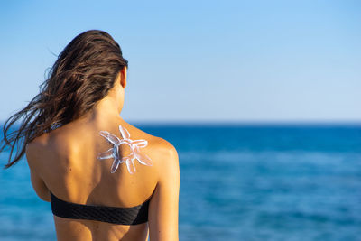 Rear view of woman standing at beach against sky