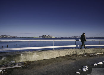 Man walking by sea in city against sky