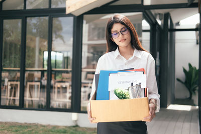 Unemployed woman carrying box while standing against office