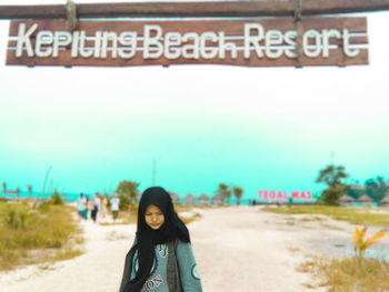 Portrait of young woman standing on street against sky