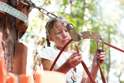 Low angle view of girl attaching safety harness on rope in forest