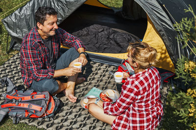 Couple having breakfast sitting by tent at camping. spending summer vacations. concept of camp life
