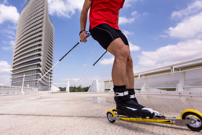 Low section of man ski rolling on road against sky