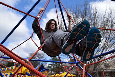 Low angle view of man sitting on play equipment at park